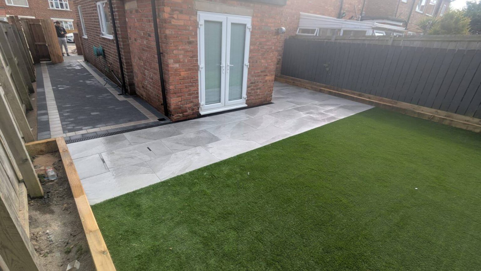 Artificial lawn beside a grey paved patio and a brick home