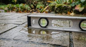 Pooled water on patio slabs with a spirit level showing an uneven fall