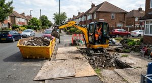 Mini digger excavating a driveway with spoil loaded into a kerbside skip