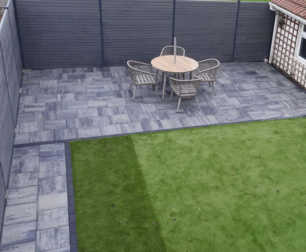 Artificial lawn beside a grey paved dining patio and dark garden fencing