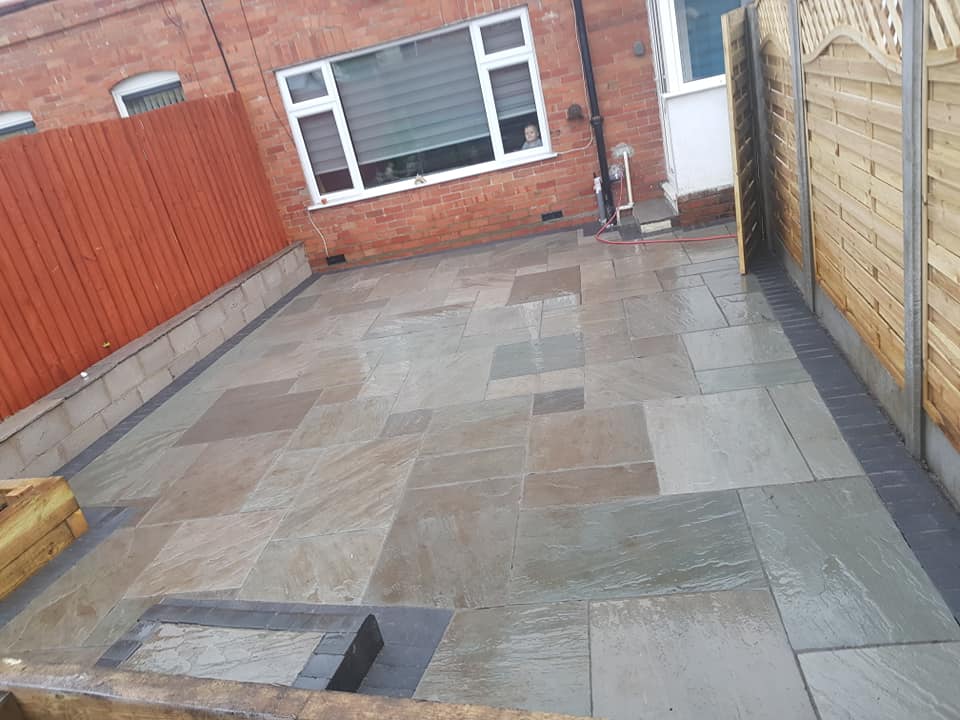 Indian sandstone patio with dark edging beside a brick house and timber fencing