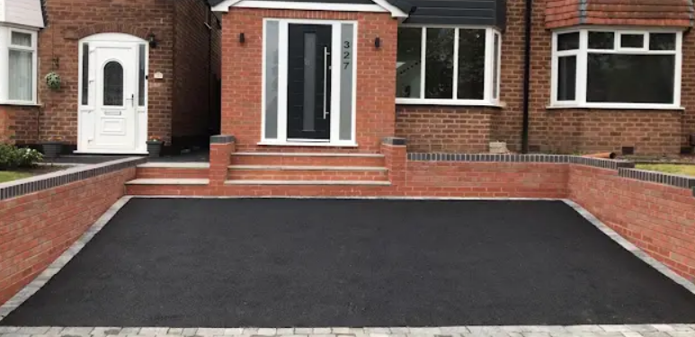 Fresh tarmac driveway leading to a brick home with steps and boundary walls