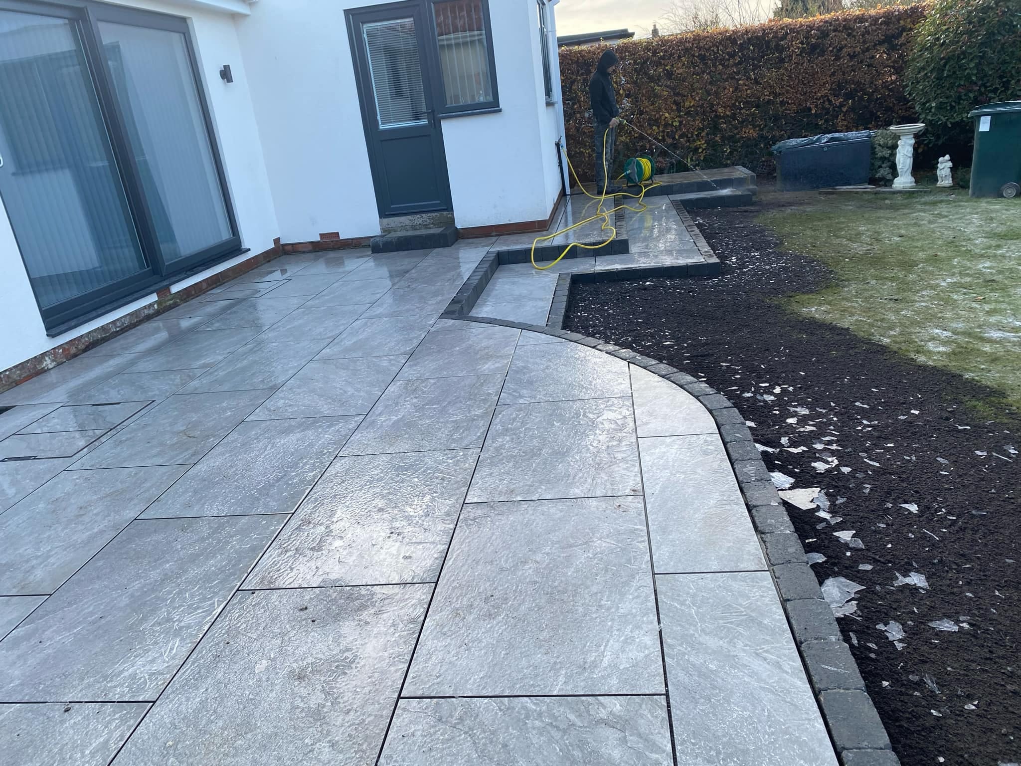 Curved grey garden patio and borders beside a white house