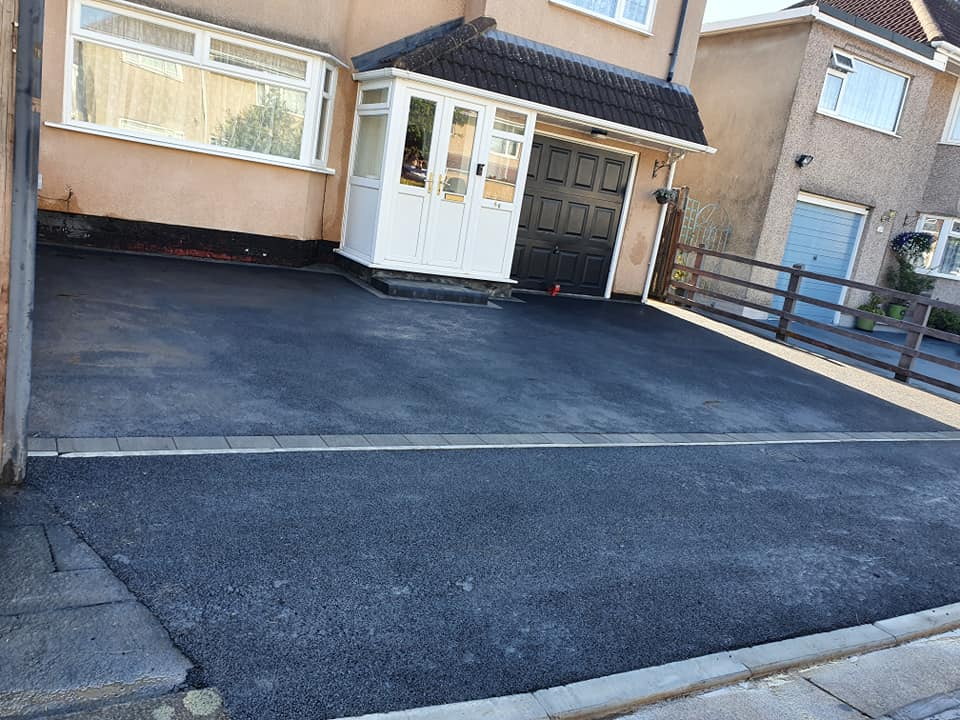Tarmac driveway with contrasting block edging outside a house with a white porch and garage
